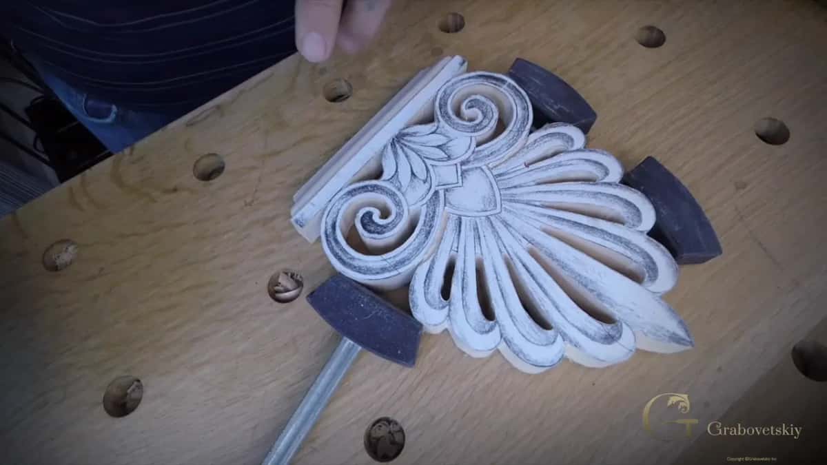 A chalked carved palmette lying on a beech bench, ringed by three black rubber-faced mallets.