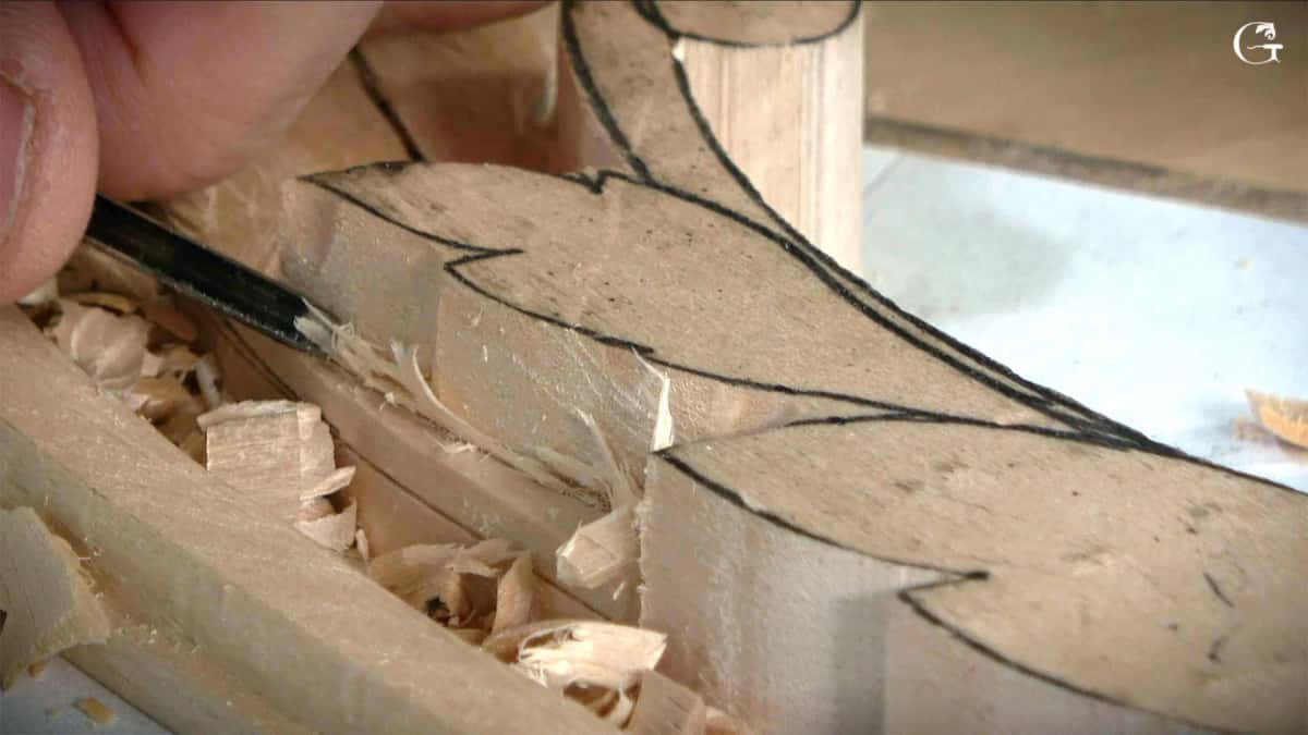 A chisel carving straight down on the drawn outline of the leaf, chips gathering around it