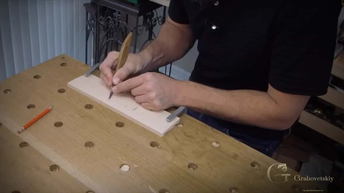 Carving a small pale board clamped flat, a pencil lying on the bench.