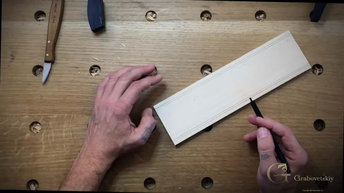 A pen draws the border line along a pale board on the bench.