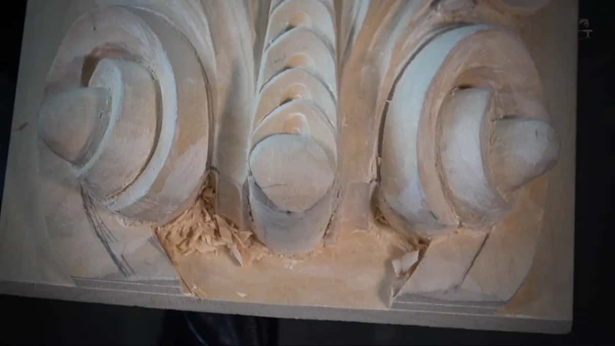 Loose chips sit in the hollow of a pale carved scroll where pencil lines still show.