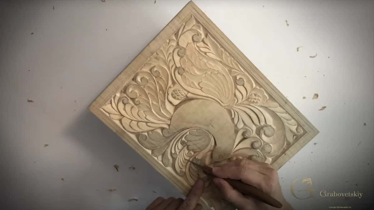 A nearly finished pale panel of leaves seen from above, a gouge in hand, chips everywhere.