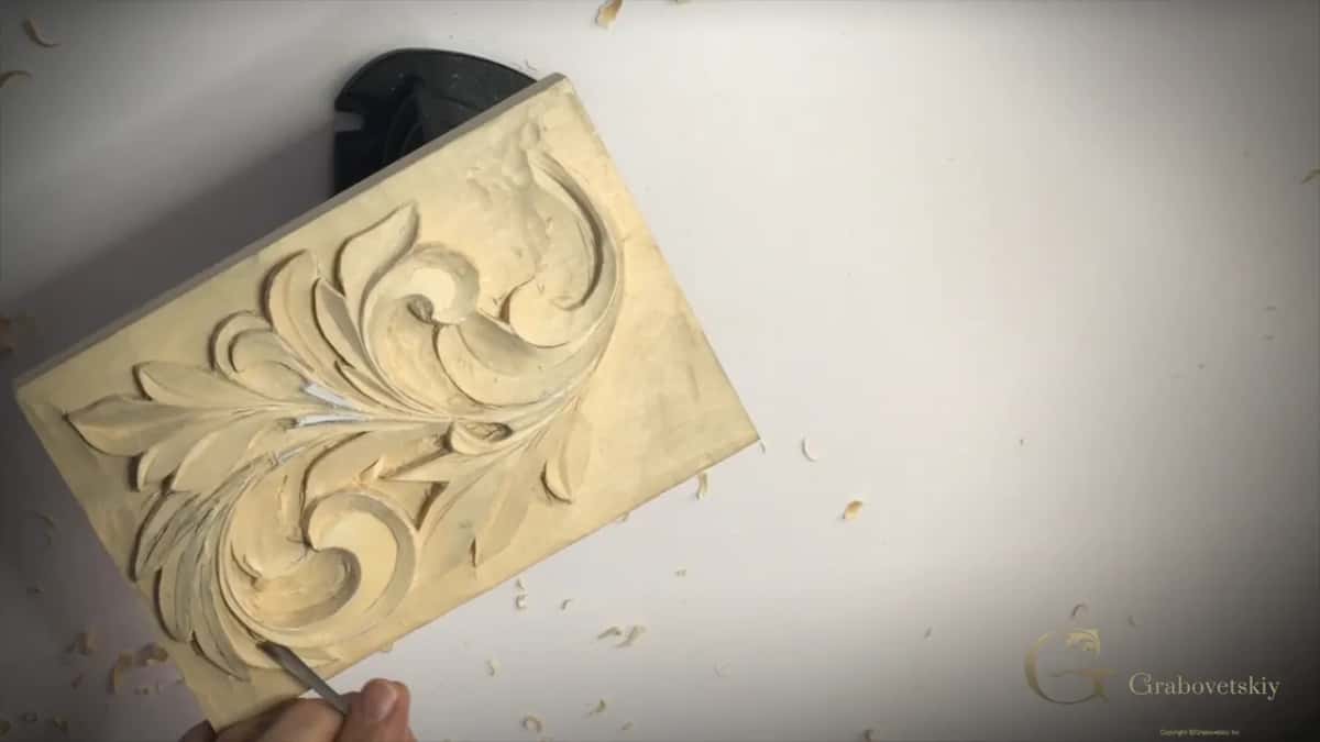 A pale scroll of acanthus stands crisp on a small panel, chips thrown across the white bench.