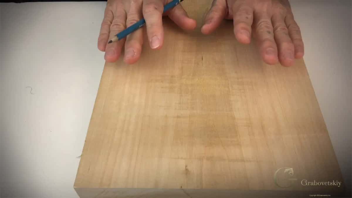 A blue pencil lies across a pale board thick enough to show its square edge.
