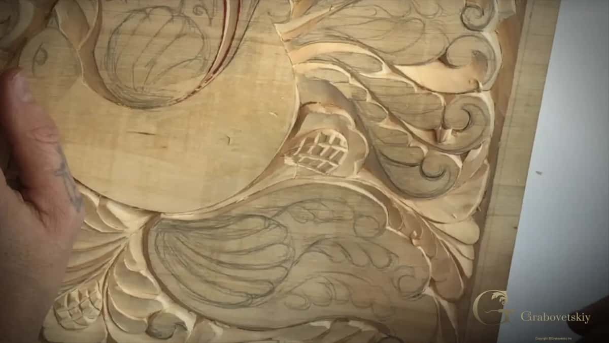 Close on a pale panel: fresh carved leaves beside pencil lines waiting their turn.