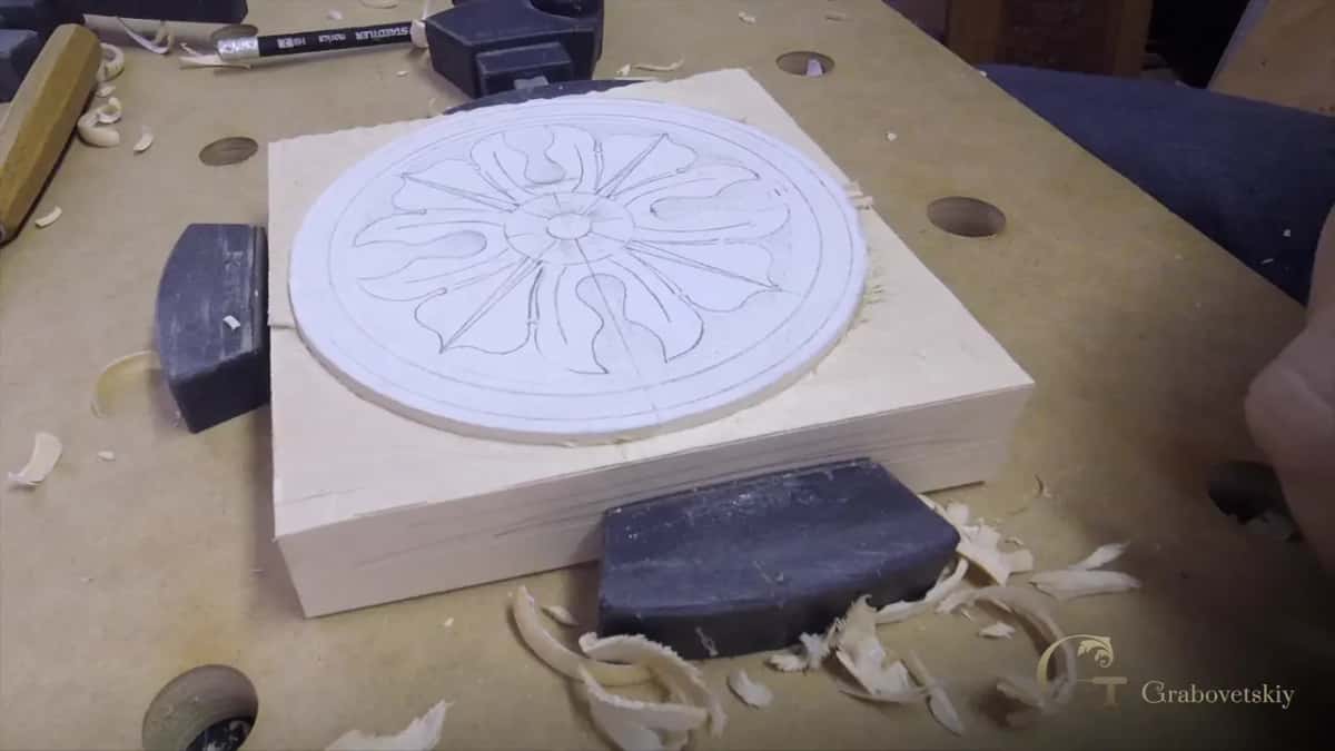 A circular rosette drawn in pencil on a thick pale block, mallet and shavings around it.