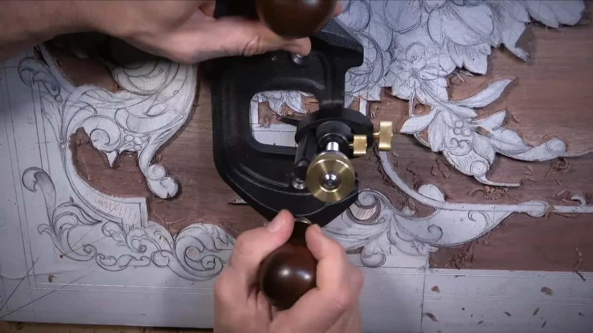 A router plane levels the ground of a dark hardwood panel drawn all over with pencil ornament.