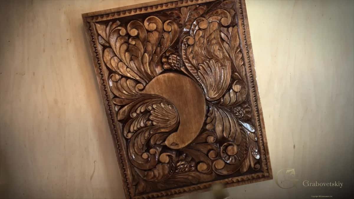 The same carved panel after a dark brown finish, hung against a pale plywood wall.