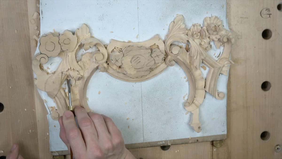Symmetrical carved cartouche of scrolls, flowers and a central shield on a pale blue painted panel under both hands