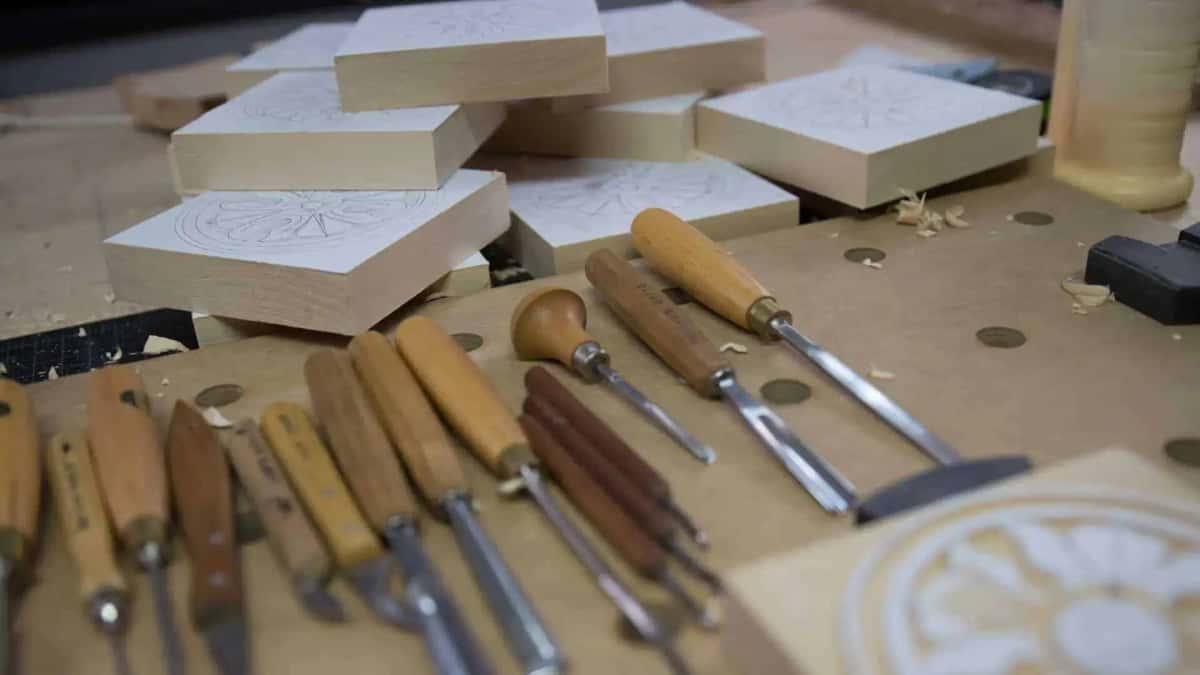 Gouges and knives in a long row with pattern marked blanks stacked behind them on the bench