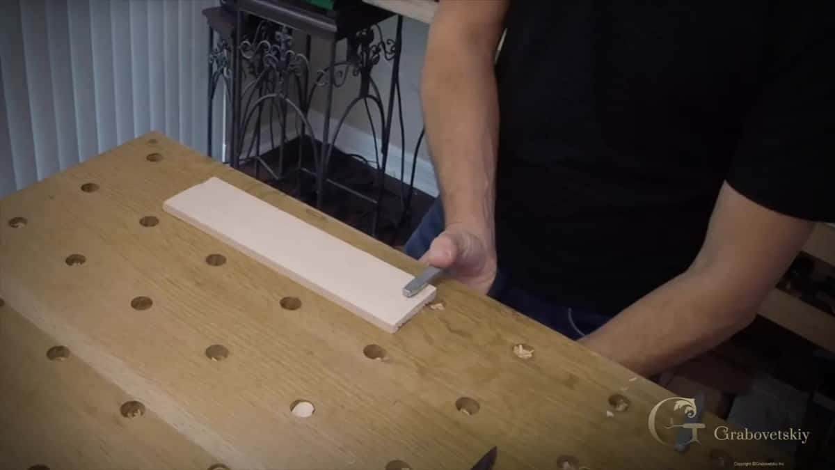 Practice board held flat on a solid table top with the carving knife brought to its near edge