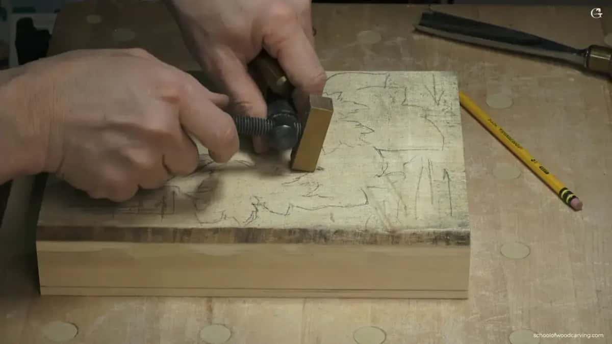 A small basswood practice panel held down with a screw clamp and bronze bench stops, a pencil lying beside it