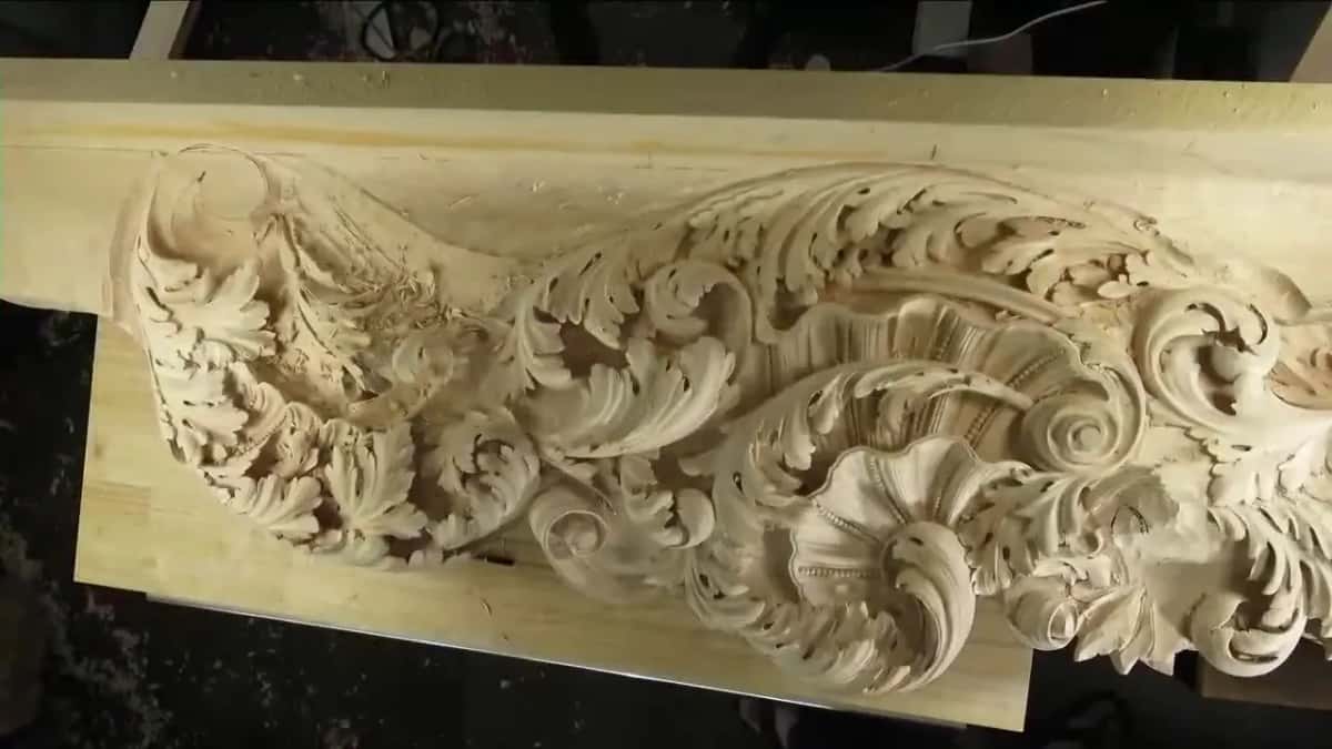 A long pale board carved with deep scrolls; the flat ground beside them shows straight grain you can barely see.