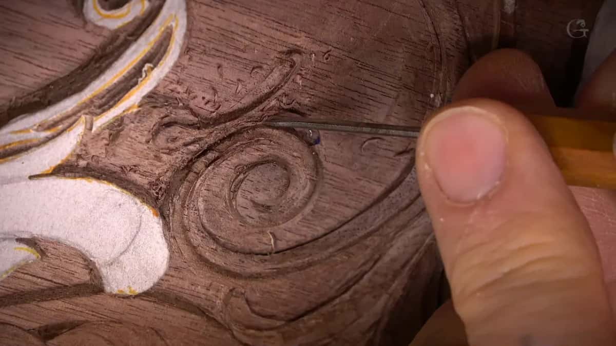 Needle thin blade laid across a carved spiral, a thumb steadying it from the side