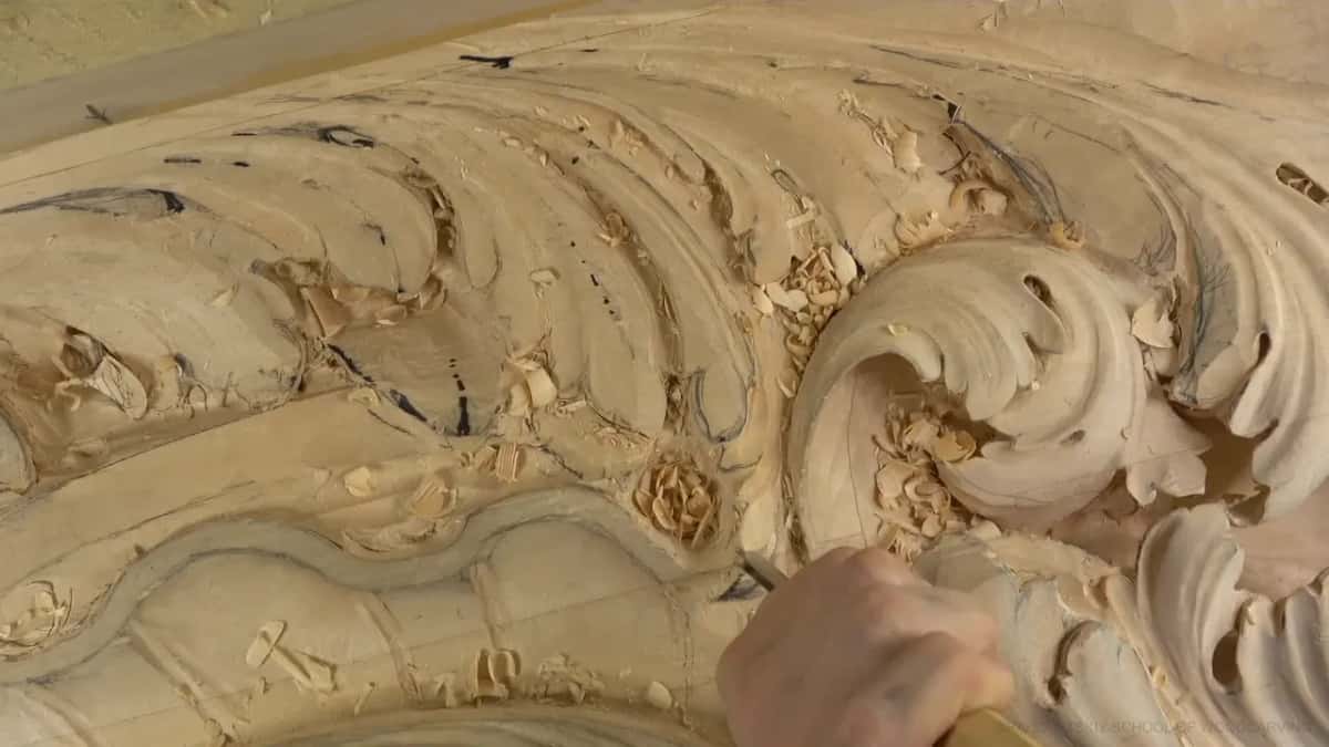 Wood chips lie all around the big carved curl, and one hand holds a handle at the bottom edge.