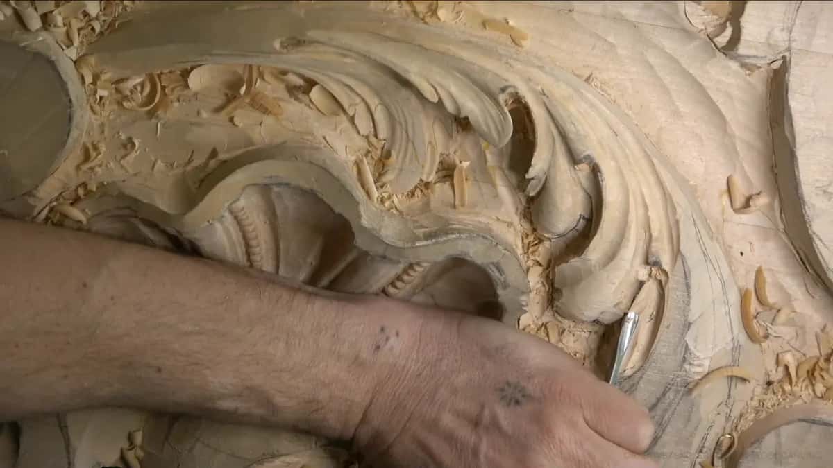 His wrist lies across the shell while a small gouge lifts wood from the lowest lobe of the leaf.