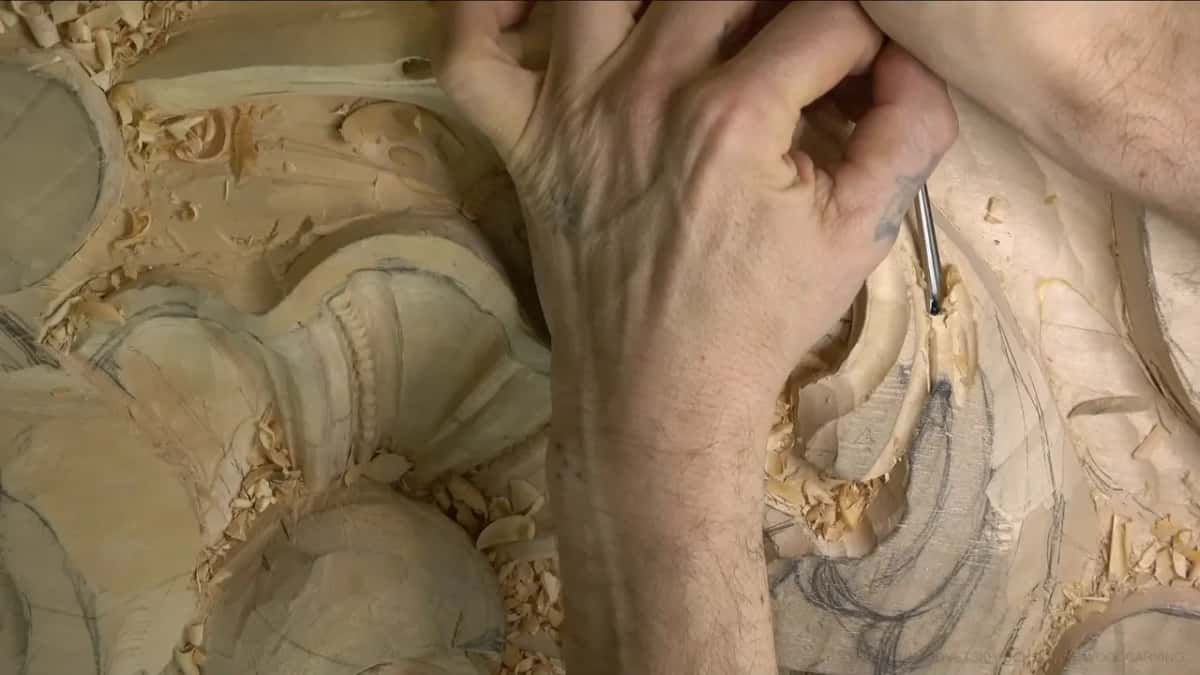 From above, a hand pushes a thin tool straight down into the lobe, the shell and beads just below it.