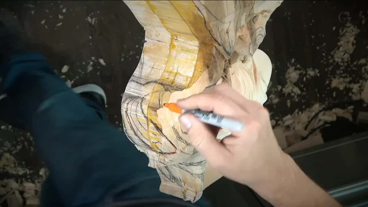 A marker with an orange cap drawing red lines over the carved block