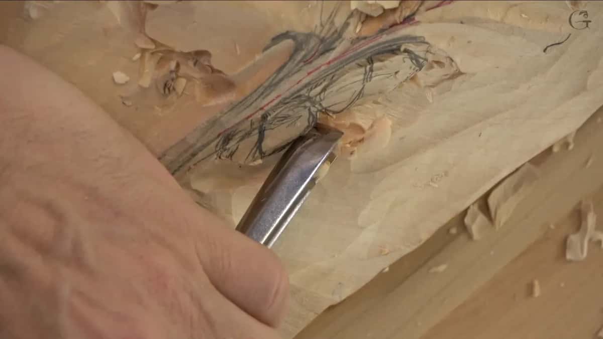 Straight gouge biting into the sketch next to the stem, chips gathering along the edge