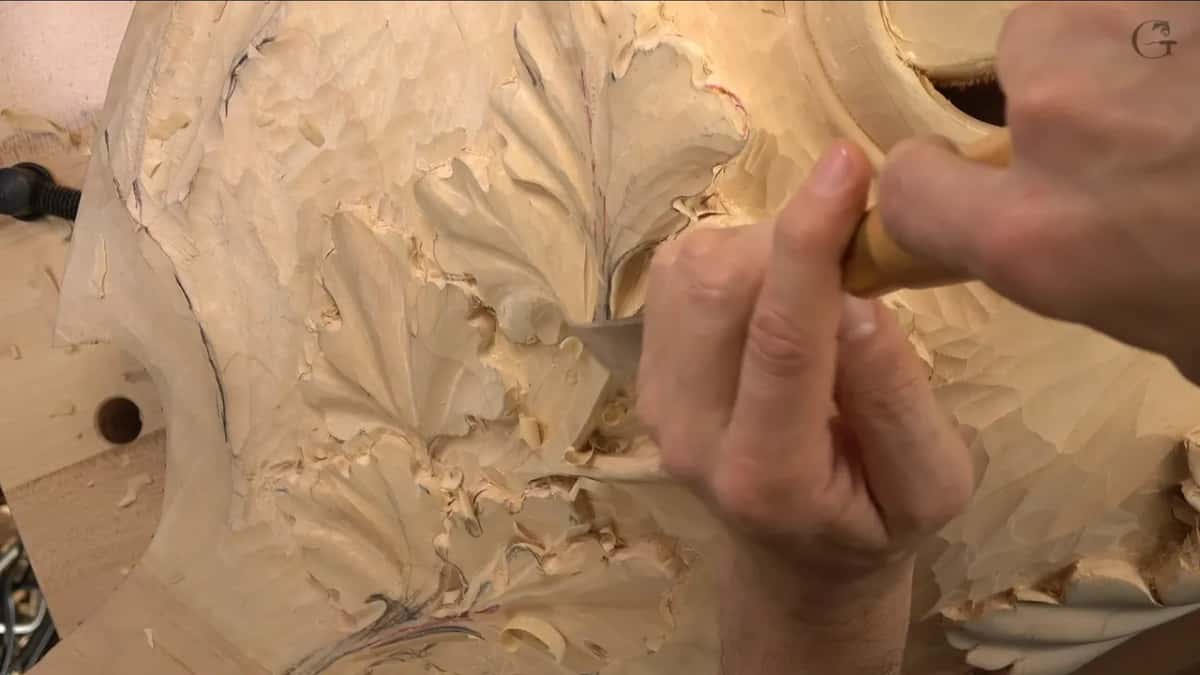 Two hands steady a gouge between the oak leaves