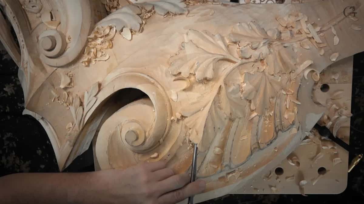 Under the oak leaves, a gouge works while the left hand holds the board