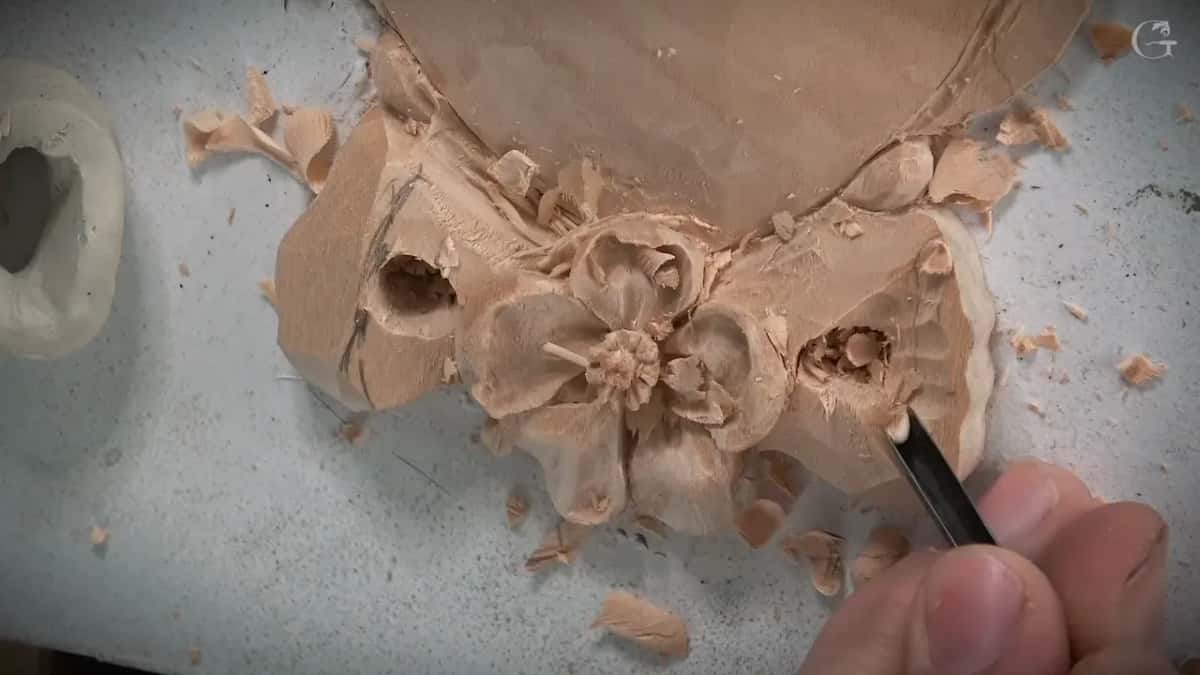 Carved bow and flower buried in shavings, a narrow blade working the right hand side