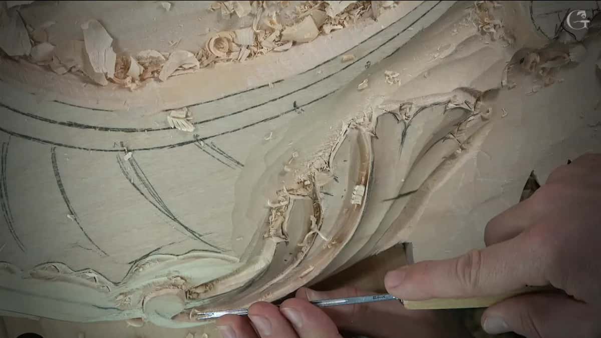 Thin veiner held in two hands inside the curved groove of the leaf, pencil lines on the plain wood above