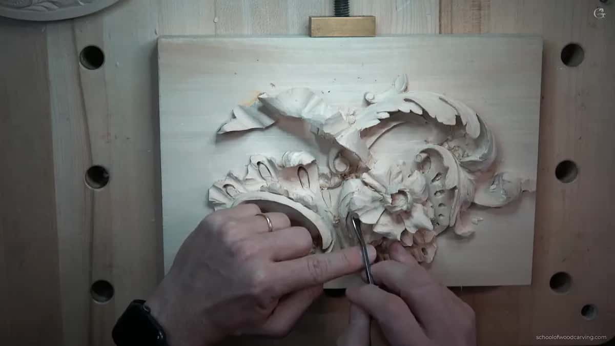Down between the big scroll and the flower, two hands close together on one slim tool