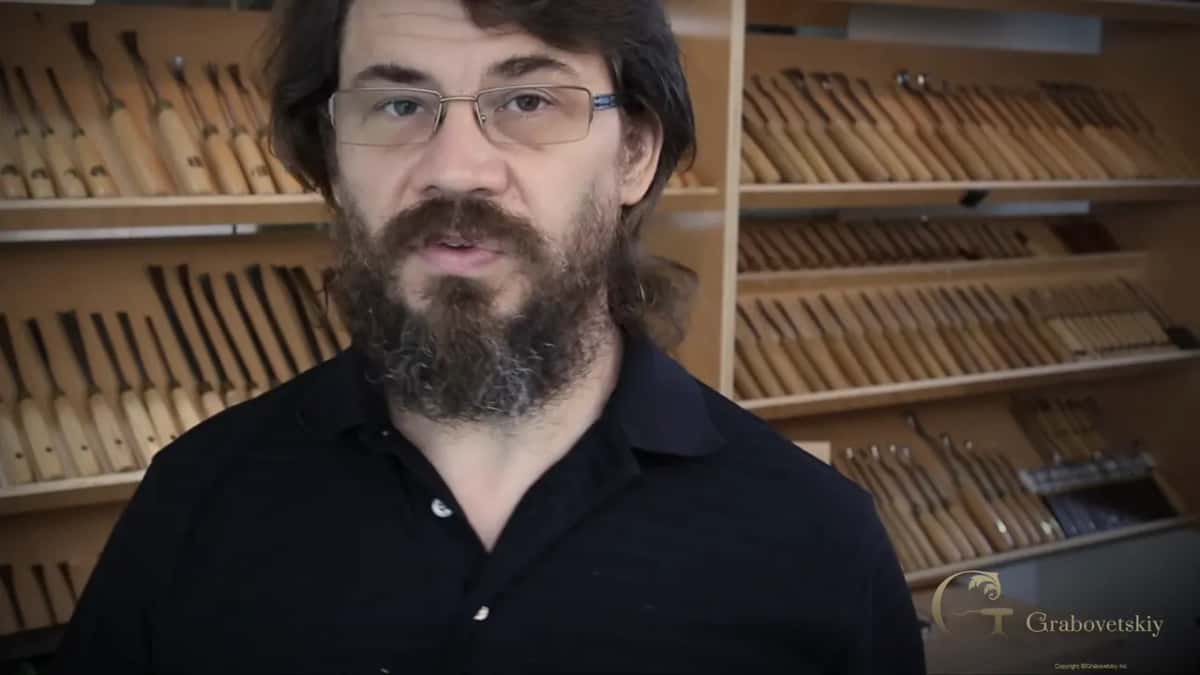 Rack of many carving tools on the wall behind him, none of which a beginner has any use for yet