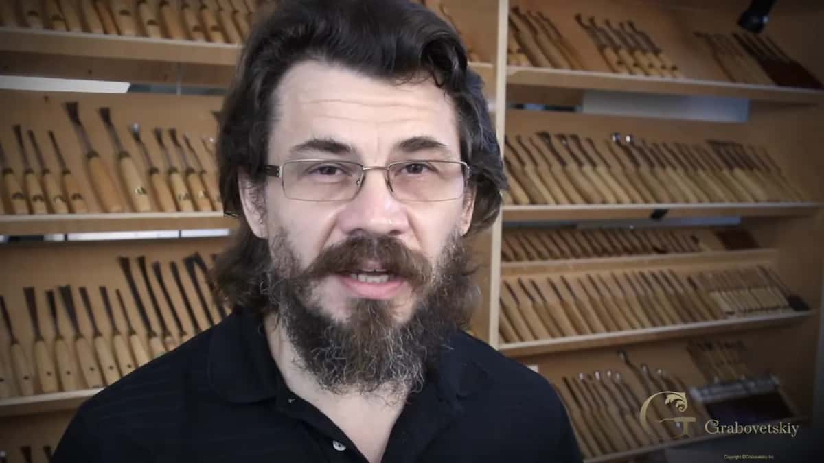 Talking to camera with a wall of carving tools racked behind him