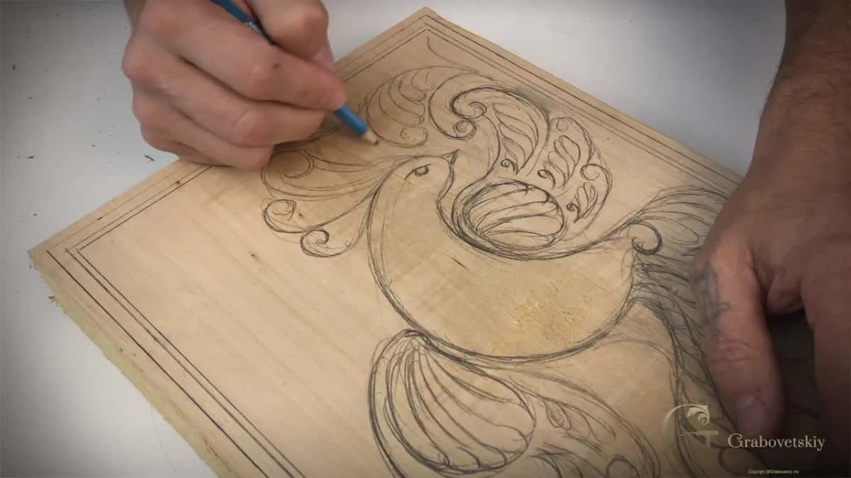 Two hands hold the tilted board while a leaf joins the curls underneath the bird's tail.