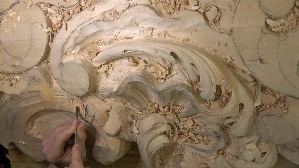 The big leaf from above, its dark hollows showing, while a hand works a small tool below.