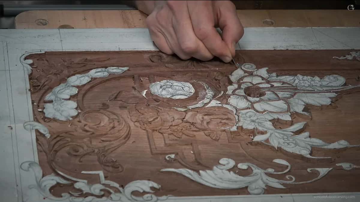 Seen from overhead, the whole ornament chalked white across walnut, one hand working right near the middle of it.