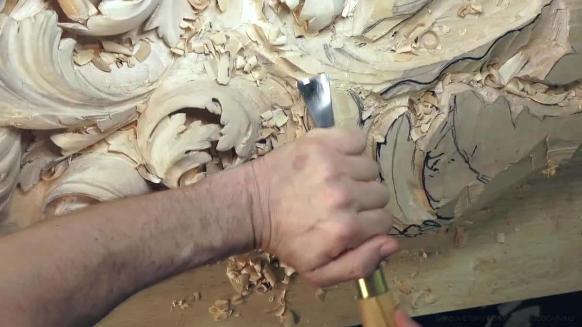 Fist around the handle, brass ferrule showing, bright blade pointed down into the leaf near the curl.