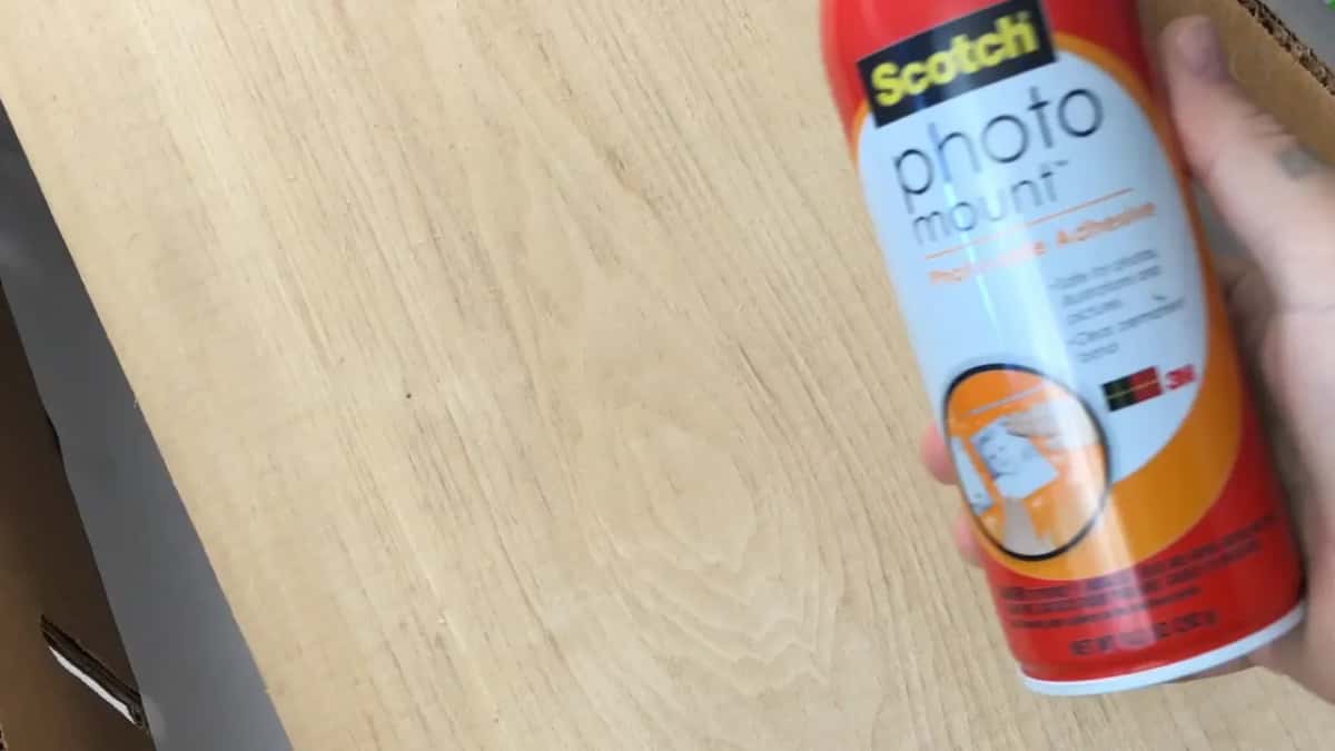 Can of photo mount spray held over a bare board