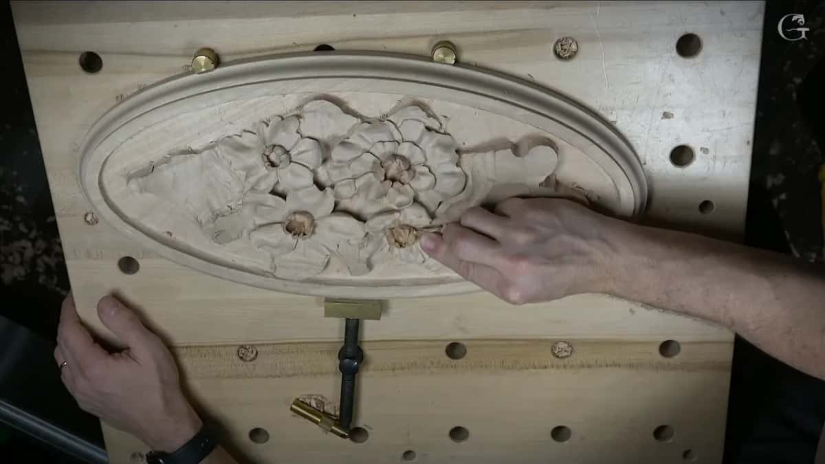 Hand on a Venetian flowers rosette in an oval frame, clamped to a bench full of holes