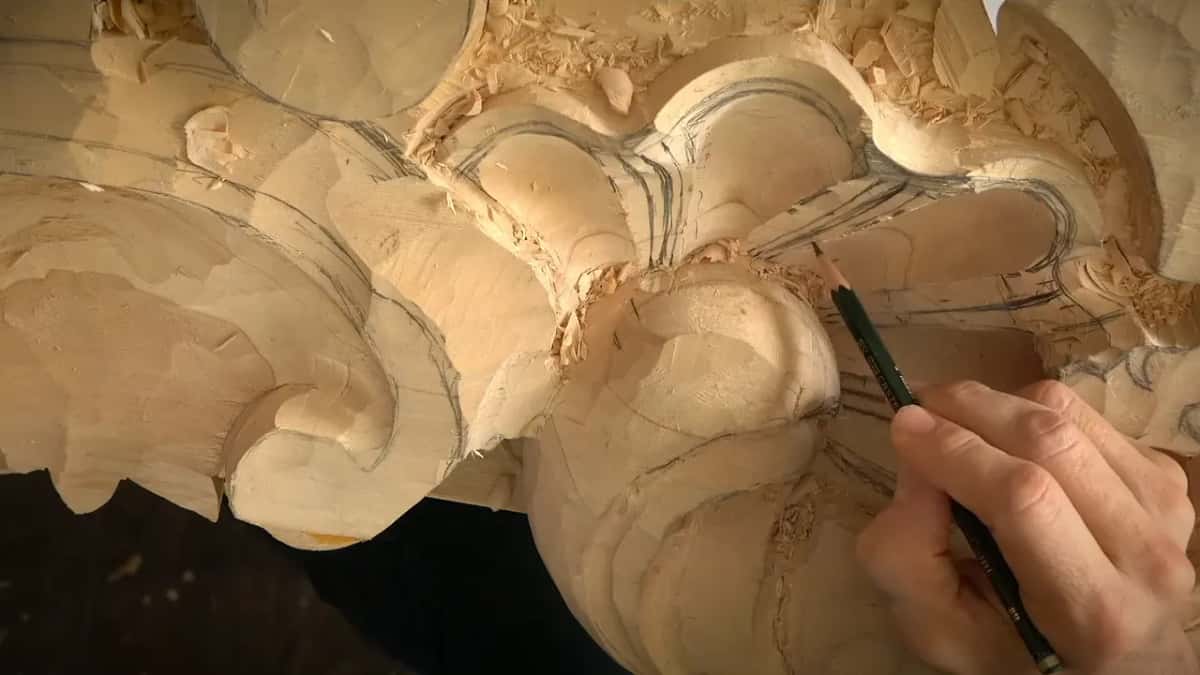 Near the round center of the shell, a hand holds a pencil low and draws over the carved ribs