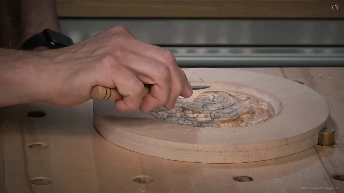 Seen from the side, one hand keeps the blade low and nearly level with the carved dish
