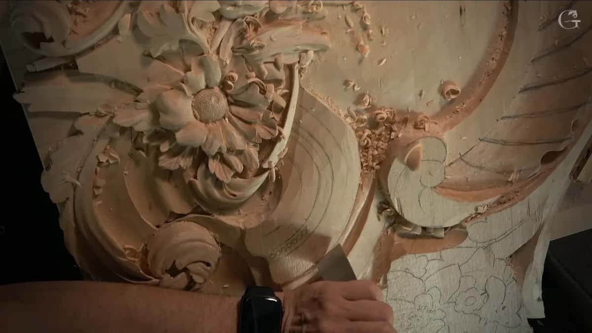 A hand with a watch holds a broad flat tool low against the curved band