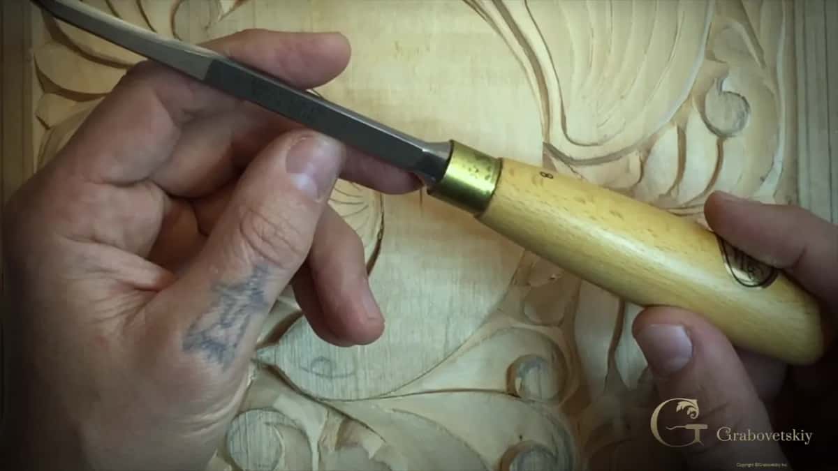 Number 8 gouge held in both hands over a carved panel, the figure 8 stamped on the pale handle.