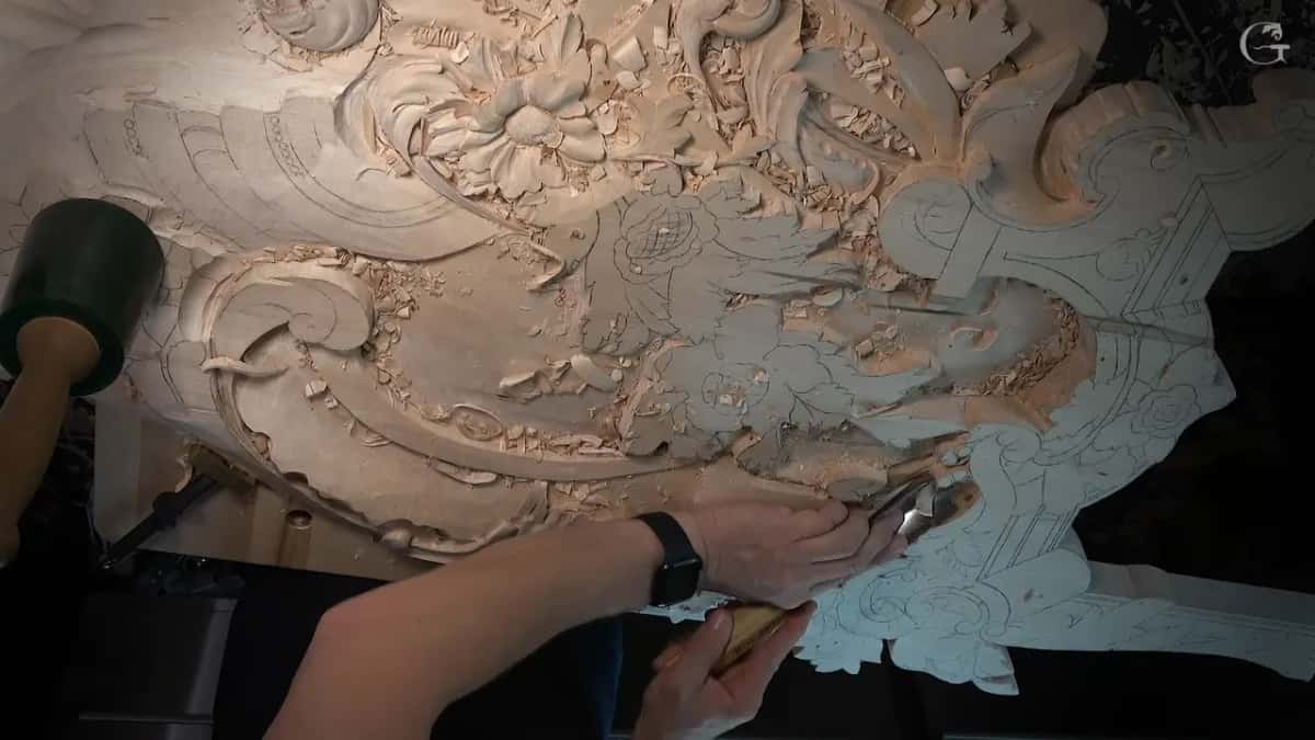 Overhead of the whole carving, a hand with a gouge at the right edge, the mallet at the left