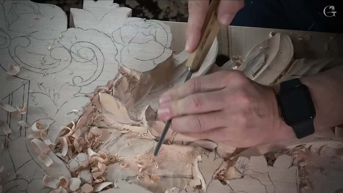 Right hand on a wood handled gouge, left fingers on its blade beside a leaf