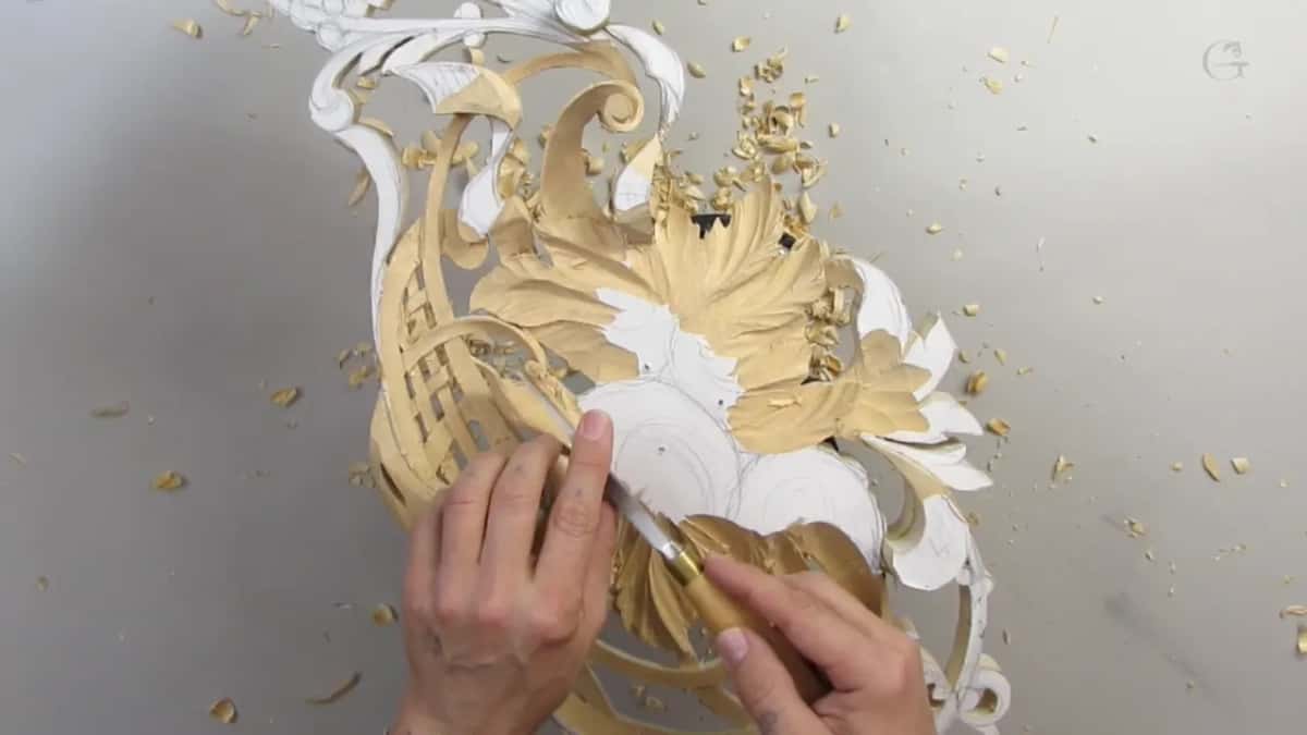 Overhead, two hands push a gouge beside the lattice and a white flower