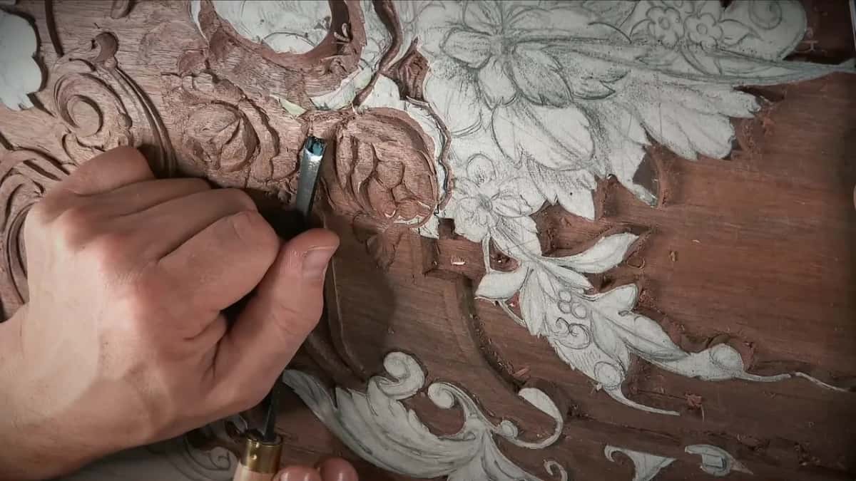 Brass ferruled tool gripped in the hand, its dark blade pressed into the carved rose