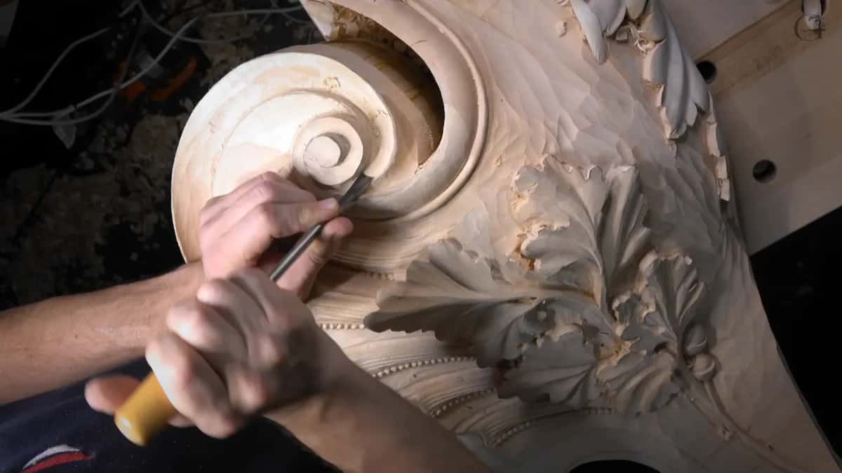 Overhead, both hands push a gouge into the hollow beside the scroll.