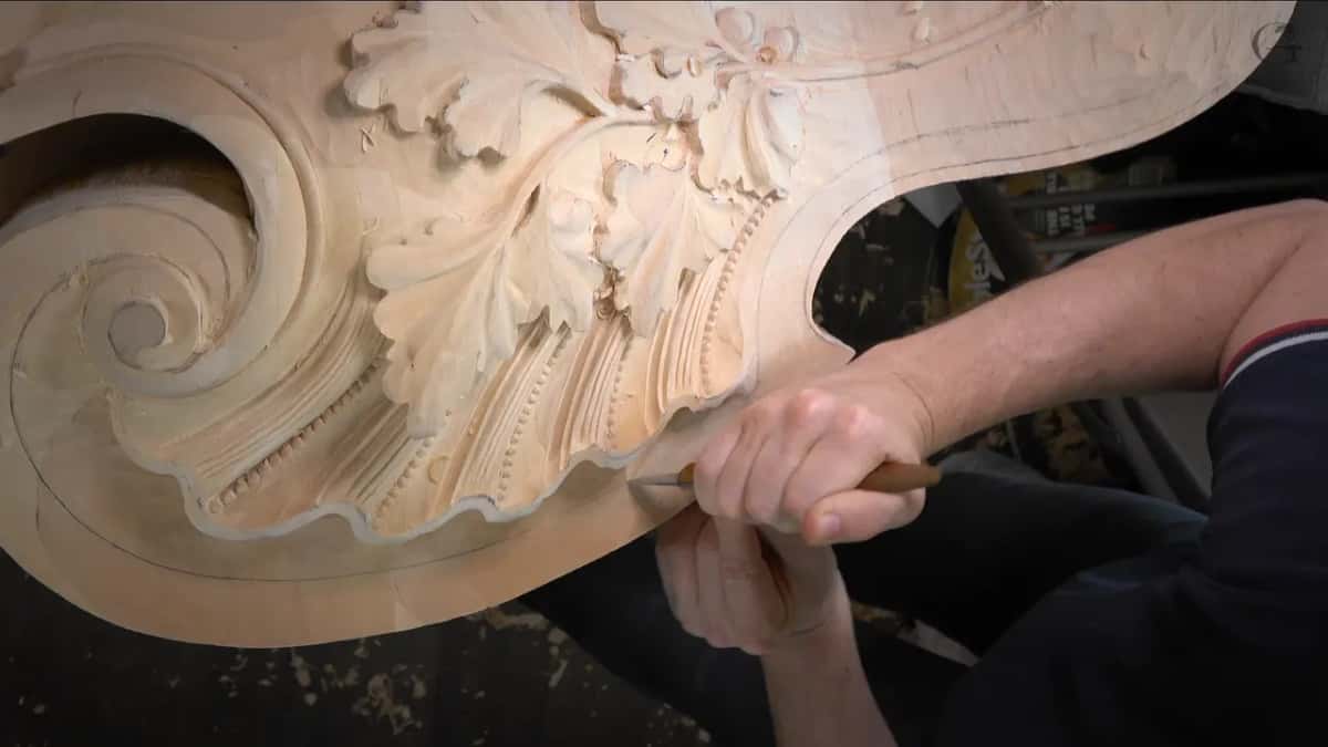 Both hands guide the knife along the rim, the fist braced against the wood.