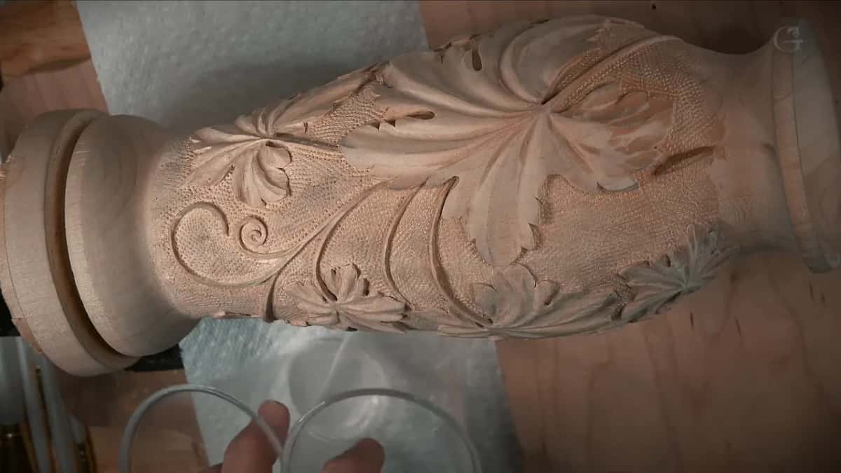 Carving finished in bare wood, leaves and a scroll over a punched background