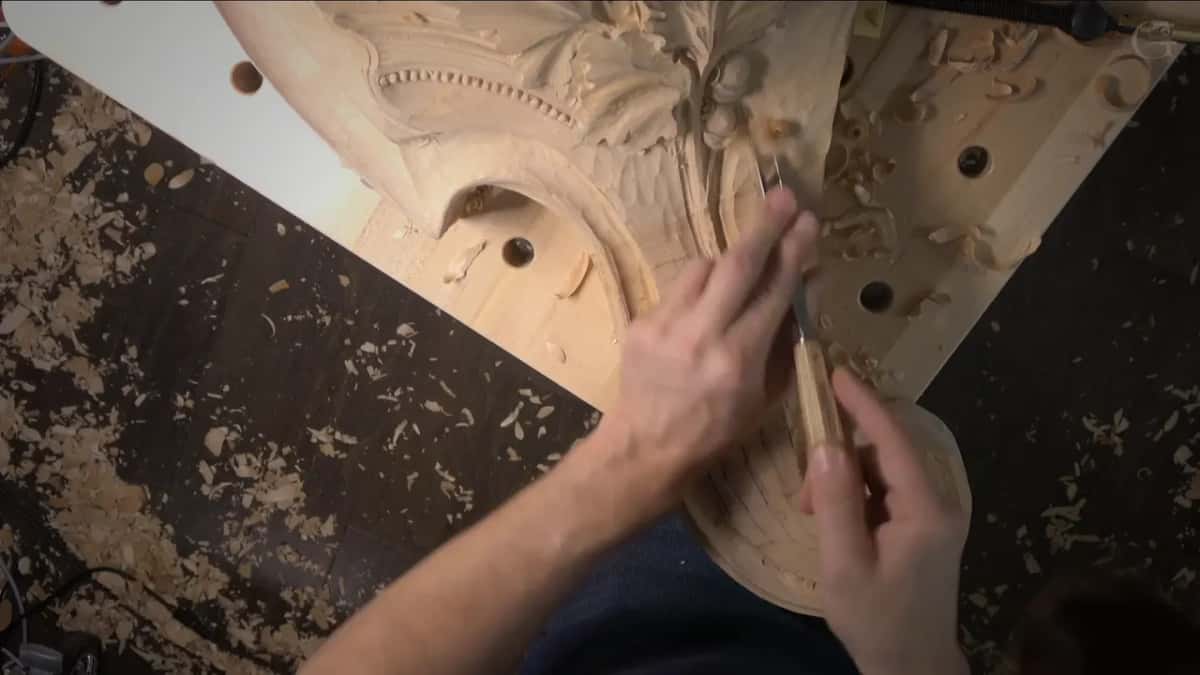 White straightedge laid beside the corbel while a gouge works