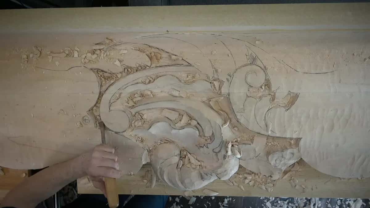 Seen from above, a gouge is held upright at the bottom edge of the carving.