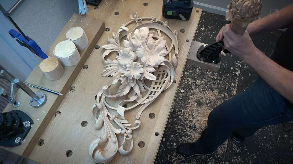 The finished panel on the workbench beside offcut discs, a carved bud on a stick in hand